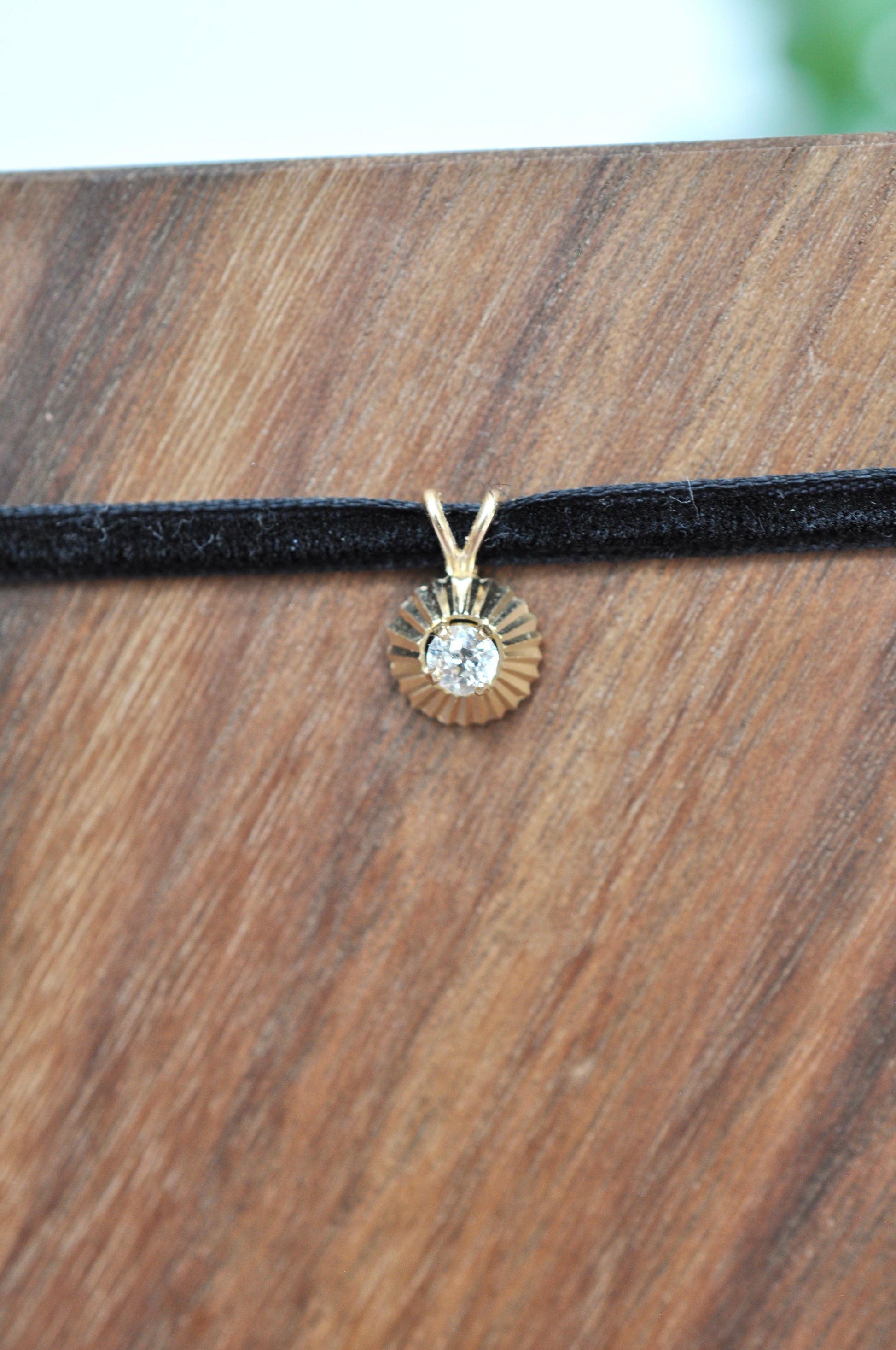 Round diamond pendant in 14kt yellow gold on a black cord against a wooden background
