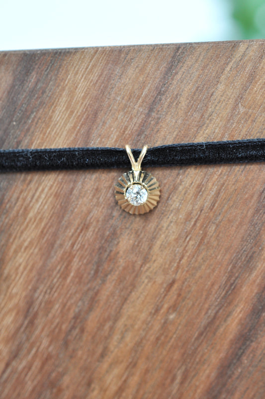Round diamond pendant in 14kt yellow gold on a black cord against a wooden background