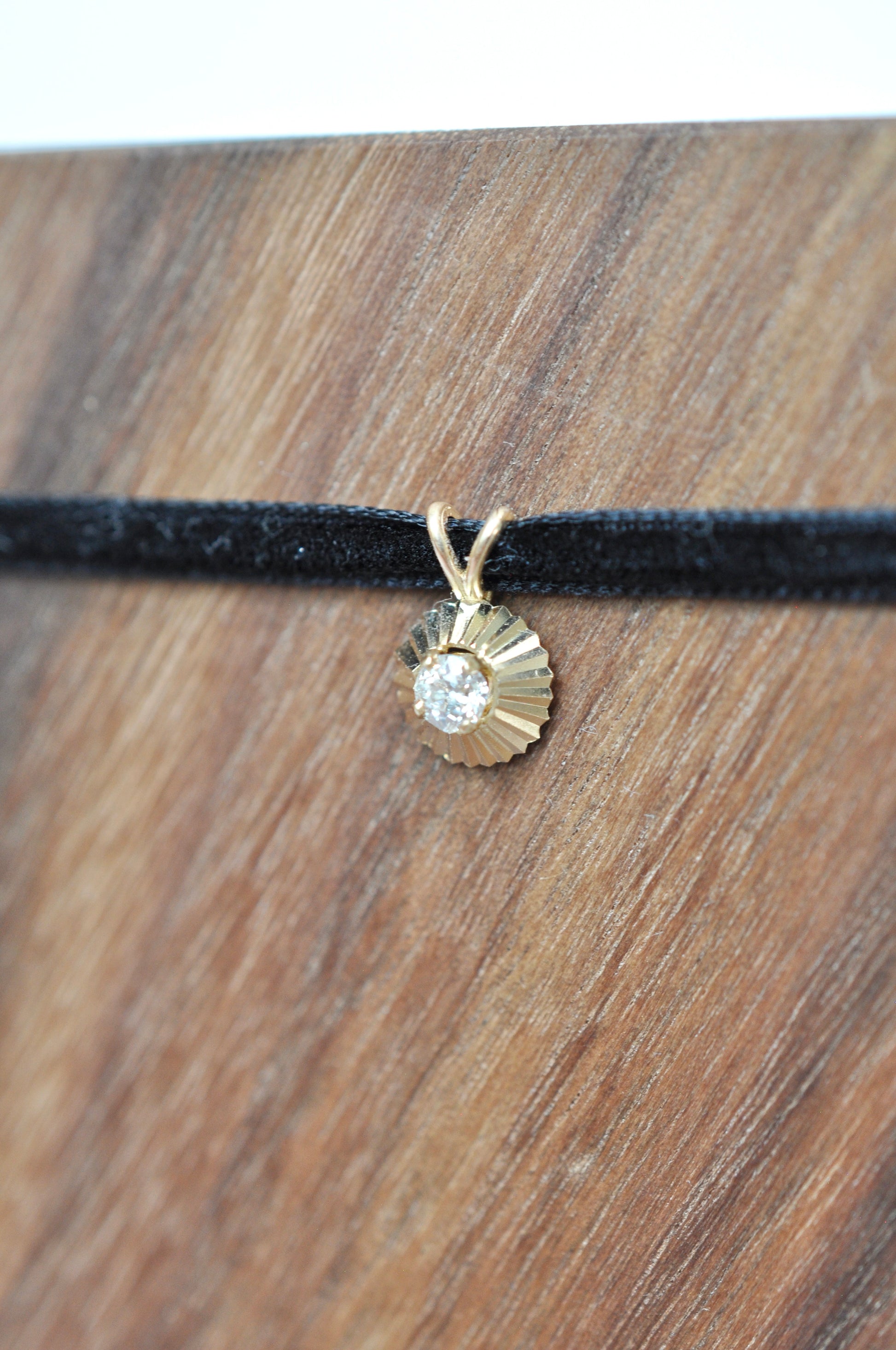 Round diamond pendant in 14kt yellow gold on a black cord against a wooden background