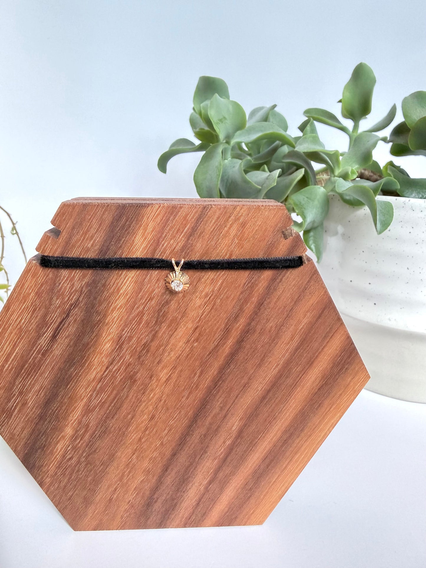 Round diamond pendant in 14kt yellow gold on a black cord against a wooden background